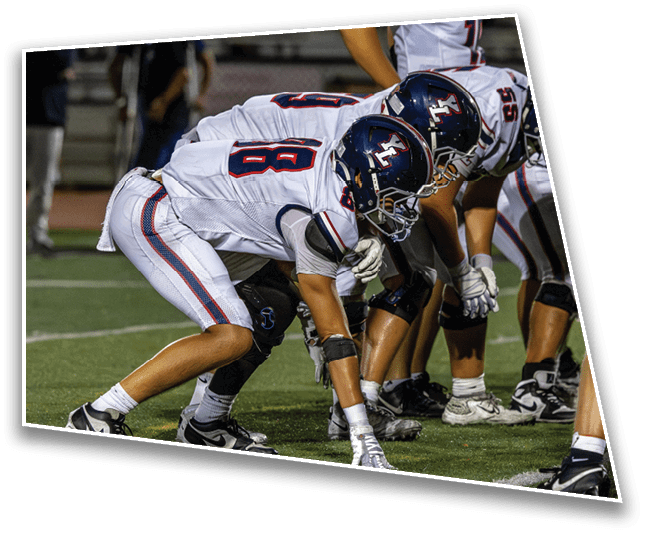Two football players in helmets and uniforms are crouched on a field in a ready stance, preparing for a play. Description generated by AI