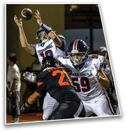 A person in a white football uniform is attempting to catch a football while another person in a black uniform with the number 21 is reaching up to block or intercept the pass during a game. Description generated by AI