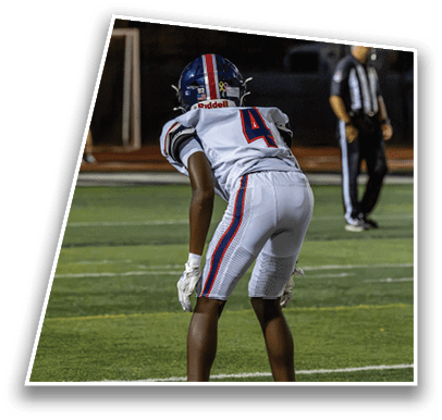 A person in a white football uniform with the number 4 is bent forward on a football field with a referee standing in the background. Description generated by AI