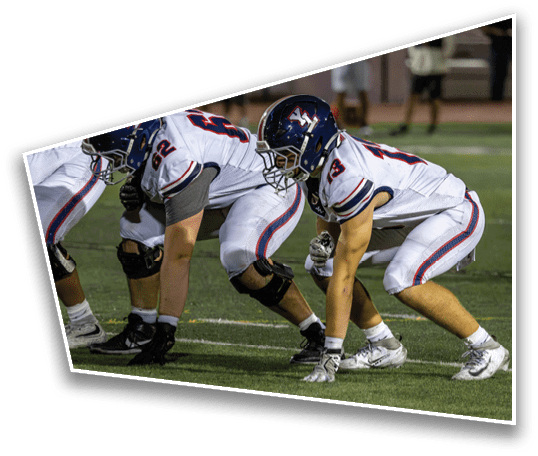 Two people in football uniforms and helmets are crouched in a ready position on a field, preparing for a play. Description generated by AI