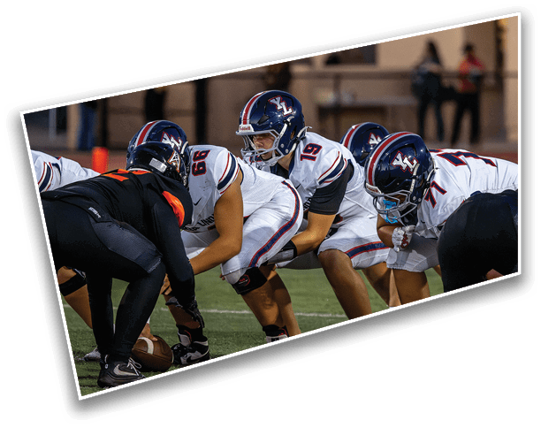 People in football uniforms are lined up on a field preparing for a play during a game. Description generated by AI