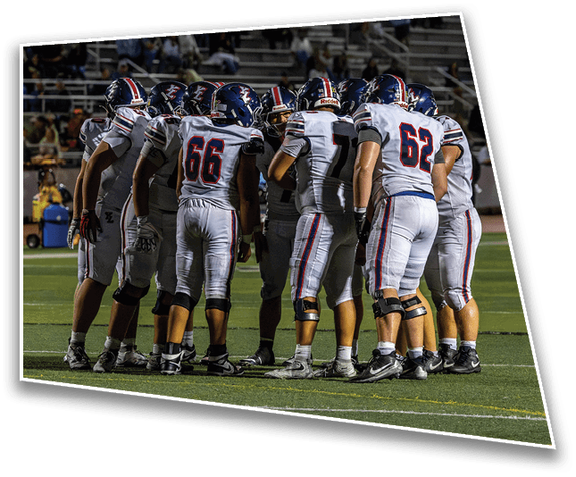 A group of football players in white uniforms with helmets are huddled together on a field during a game. Description generated by AI
