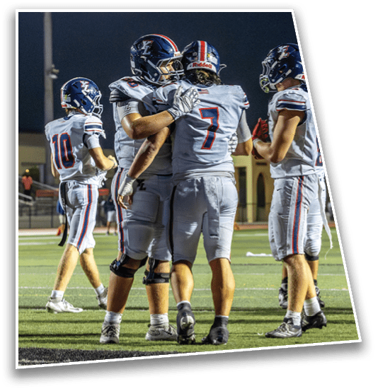 Four people in football uniforms and helmets stand on a field at night with two of them embracing. Description generated by AI