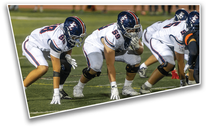 Several people in football uniforms are crouched in a ready position on a field, preparing for a play. Description generated by AI