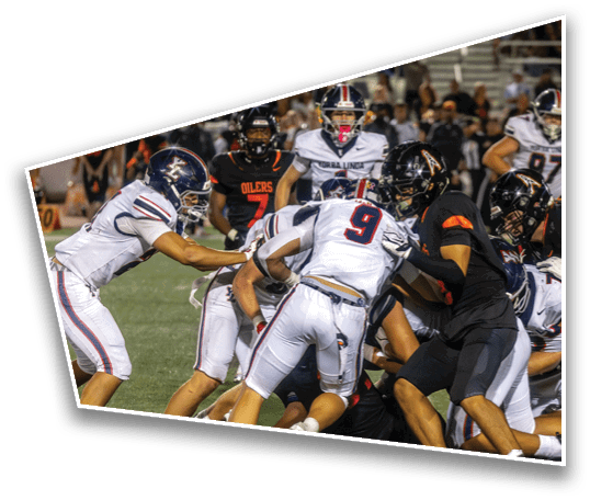 People wearing football uniforms are engaged in a close play on a grassy field during a game. Description generated by AI