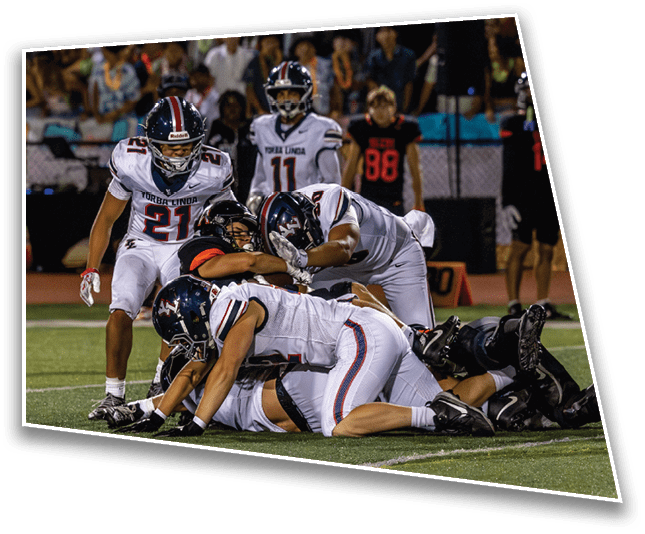Several people in football uniforms are engaged in a tackle on a field during a game. Description generated by AI