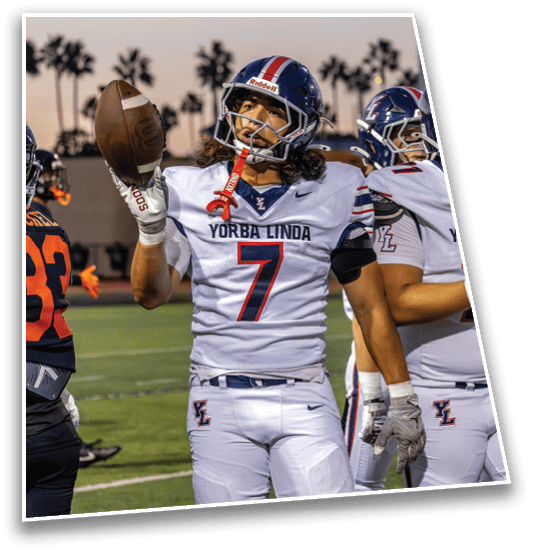 A person wearing a white football uniform with the number seven and “Yorba Linda" on the jersey is holding a football on a field with other players in the background. Description generated by AI