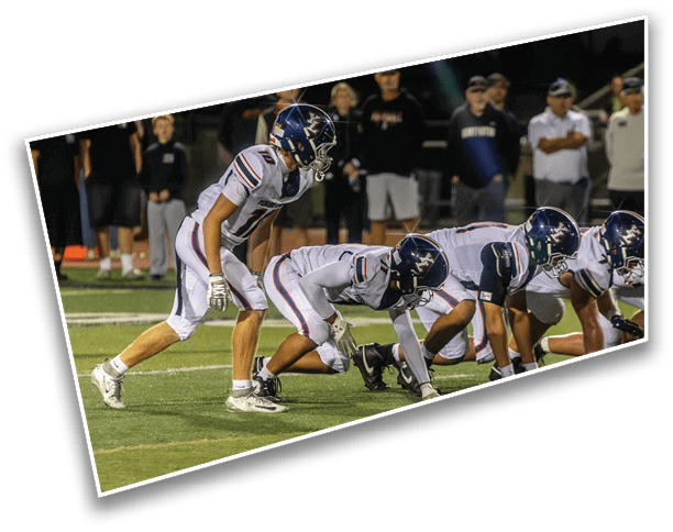A person in a football uniform and helmet is leaning forward on a field at night with a group of people standing in the background. Description generated by AI