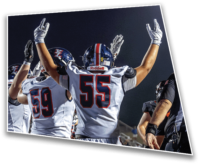 People wearing football uniforms with helmets and gloves raise their arms in celebration on a field at night. Description generated by AI