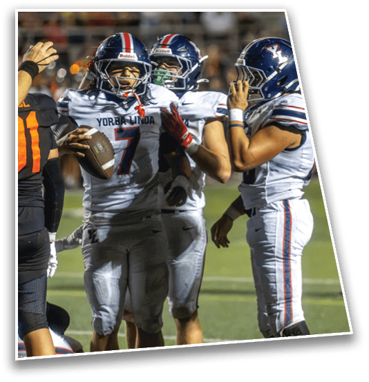 Three people in football uniforms are on a field with one holding a football and the others appearing to communicate or celebrate. Description generated by AI