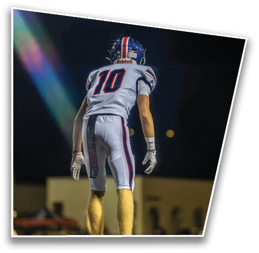 A person wearing a white sports uniform with the number 10 stands on a grassy field at night with another person in the background. Description generated by AI