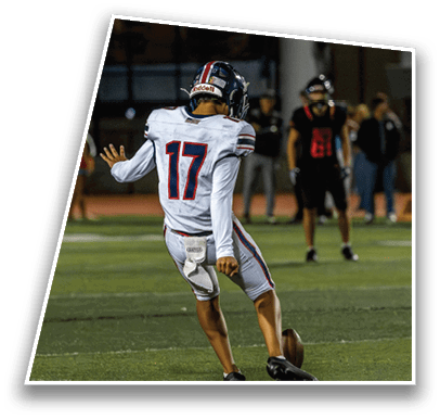 A person wearing a football helmet and white jersey is seen from behind on a dimly lit field at night. Description generated by AI
