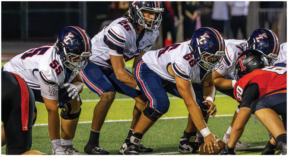 Several people in football uniforms are positioned on a field, appearing ready for a play during a nighttime game. Description generated by AI