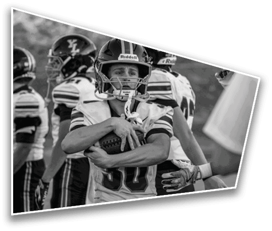 A group of people wearing football helmets and uniforms are standing together with one person holding a football tightly. Description generated by AI