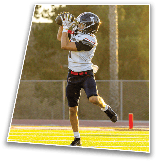 A person in a football uniform is jumping and catching a football on a sunlit field near the end zone. Description generated by AI