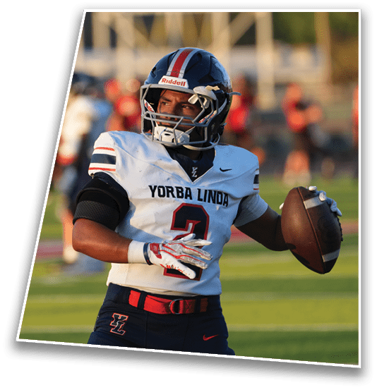 A person wearing a Yorba Linda football uniform is preparing to throw a football on a field during a game. Description generated by AI