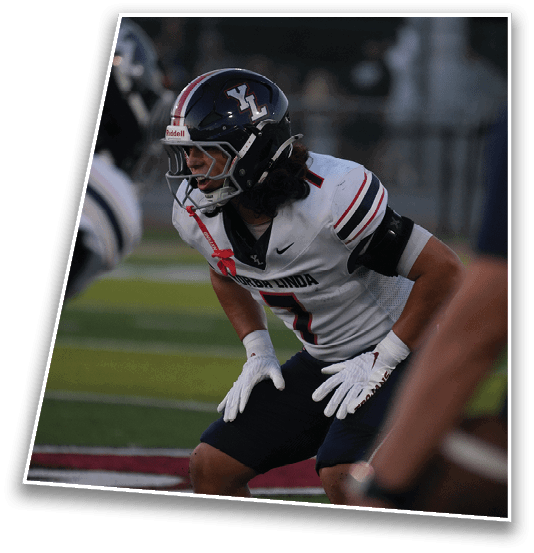 A person wearing a dark football helmet with “YL" on the side and a white jersey with red and blue stripes is captured in action during a game. Description generated by AI