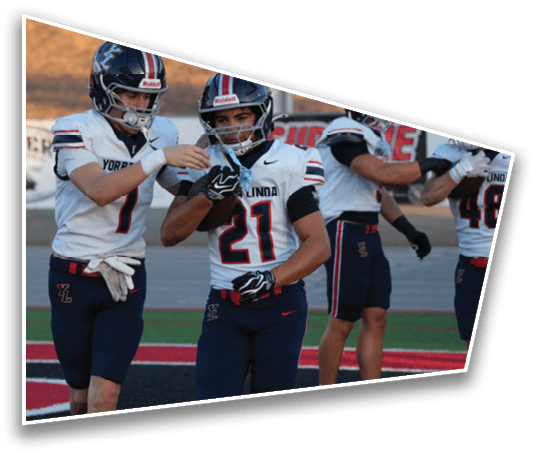 Two people in football uniforms are standing on a field with one person handing a football to the other. Description generated by AI