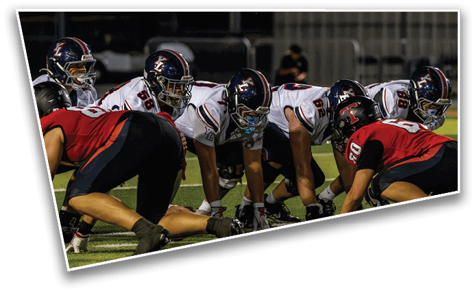 Two opposing American football teams are lined up facing each other on the field, preparing for the next play. Description generated by AI