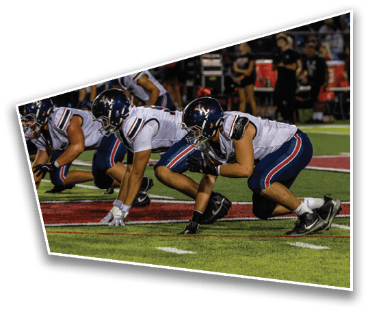 Four football players in white jerseys and helmets are crouched in a ready position on a green field during a game. Description generated by AI