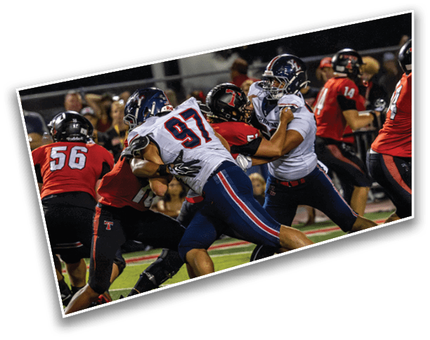 Several people wearing football uniforms are engaged in a play on a football field during a game at night. Description generated by AI