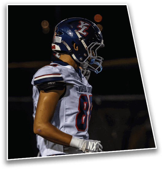 A person wearing a football helmet and white jersey with the number 81 stands on a field at night. Description generated by AI