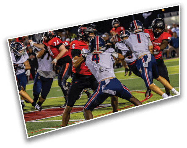 Two teams of football players in red and white uniforms are actively engaged in a game on a field under stadium lights. Description generated by AI