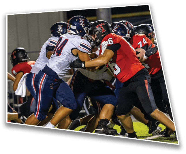 People wearing football helmets and uniforms are engaged in a close formation on a field at night. Description generated by AI
