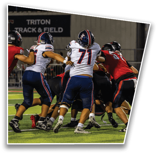 Several people wearing football uniforms are engaged in a play on a field with a “TRITON TRACK & FIELD" sign visible in the background. Description generated by AI