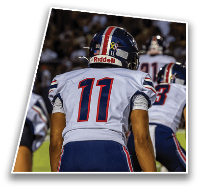 A person wearing a white football jersey with the number 11 and a helmet is standing on a field with other players in the background. Description generated by AI
