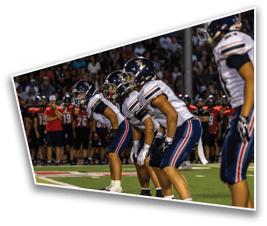 Three people in football uniforms and helmets are crouched in a ready position on a field with a crowd in the background. Description generated by AI