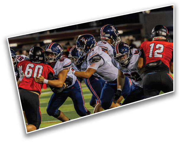 Several people wearing football uniforms are engaged in a play on a football field under stadium lights. Description generated by AI
