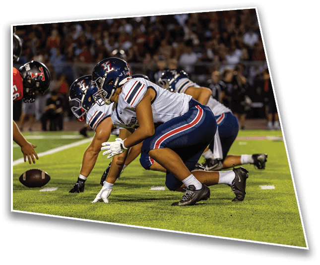 Three people in football uniforms are crouched on a field in a ready stance, preparing for a play during a game. Description generated by AI