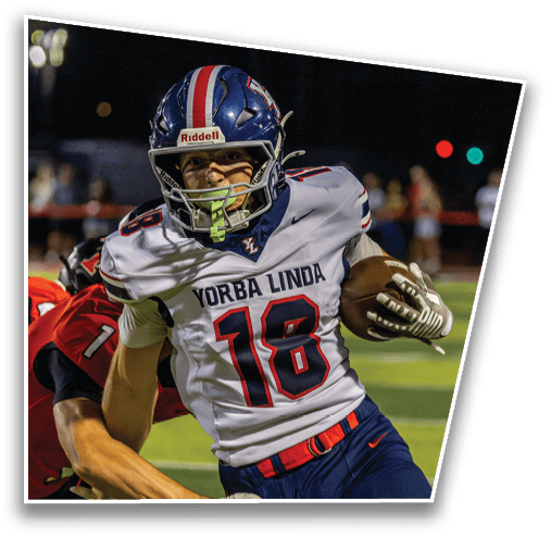 A person wearing a Yorba Linda football uniform with the number 18 is running with a football during a nighttime game. Description generated by AI