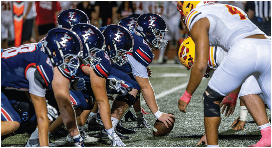 People in football uniforms are lined up on a field facing each other, preparing for a play. Description generated by AI