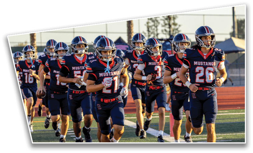 A group of people wearing matching football uniforms with helmets are running together on a sports field during daylight. Description generated by AI