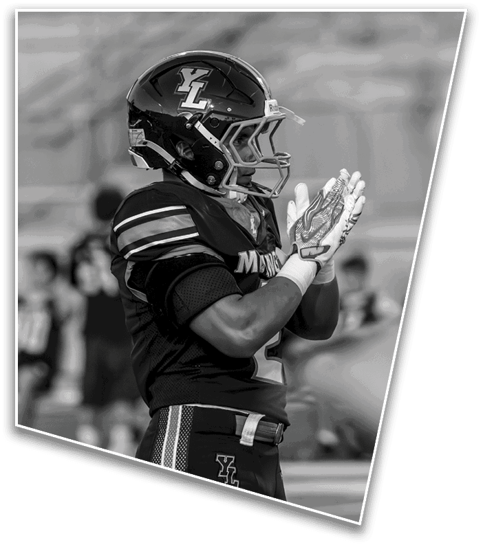 A person wearing a football uniform and helmet is standing on a field clapping their hands. Description generated by AI