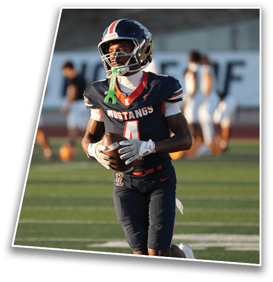A person wearing a football uniform with the word Mustangs and the number 4 is holding a football on a field during a game. Description generated by AI