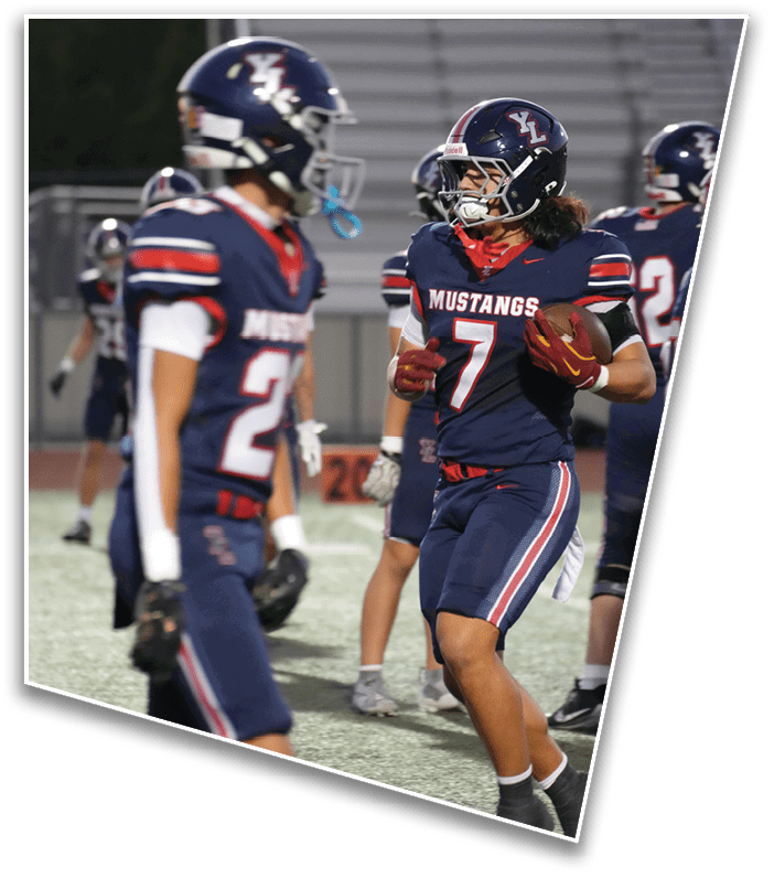 Two football players in navy blue uniforms with red and white accents and helmets are engaged in conversation on the field. Description generated by AI