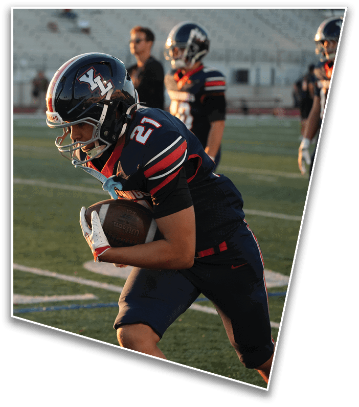 An adult wearing a football uniform and helmet is running on a field while holding a football securely. Description generated by AI