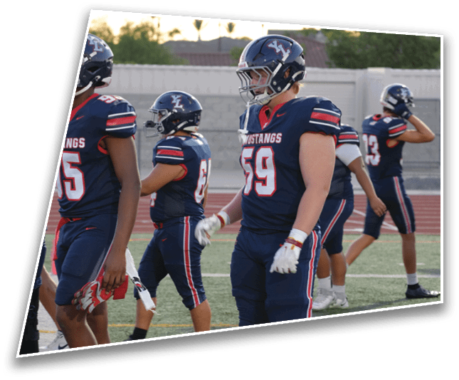 Several people in football uniforms and helmets stand on a field, some holding gloves and others adjusting helmets. Description generated by AI