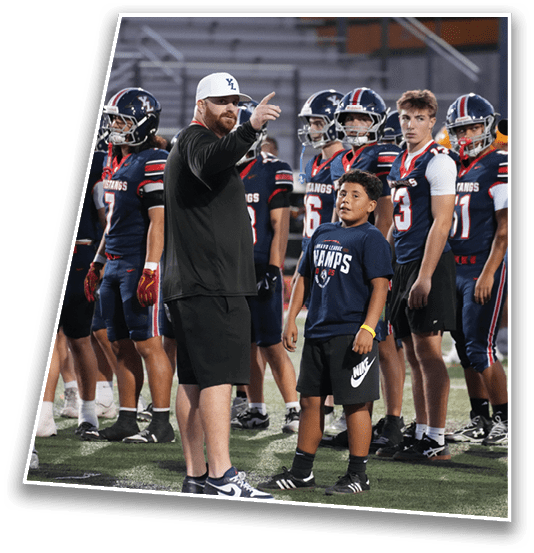 An adult wearing a white cap and black shirt is pointing while standing among a group of people in football uniforms and a child wearing a navy blue shirt with text. Description generated by AI