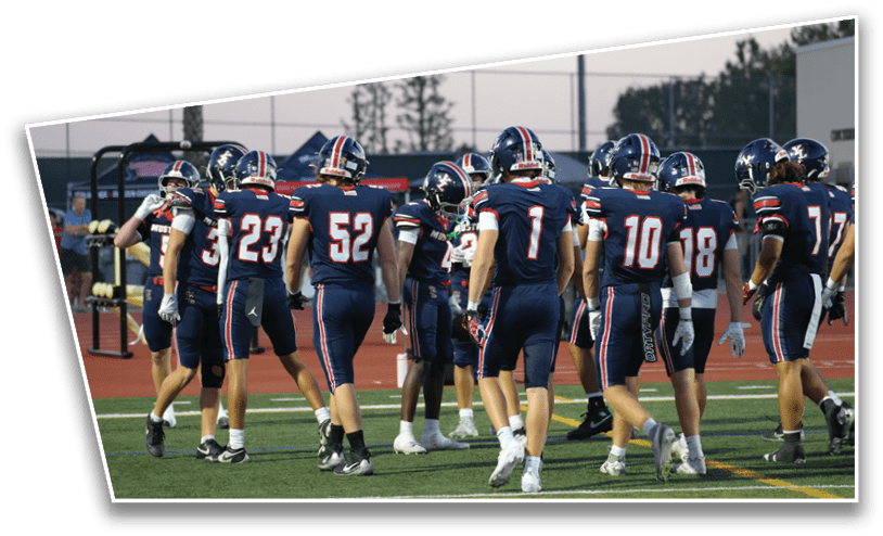 A group of people wearing navy blue football uniforms with red and white stripes are gathered on a field, facing away from the camera. Description generated by AI