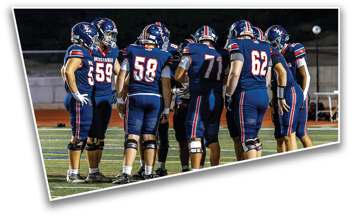 A group of people wearing blue football uniforms with helmets are standing together on a field, seemingly in a huddle during a game. Description generated by AI