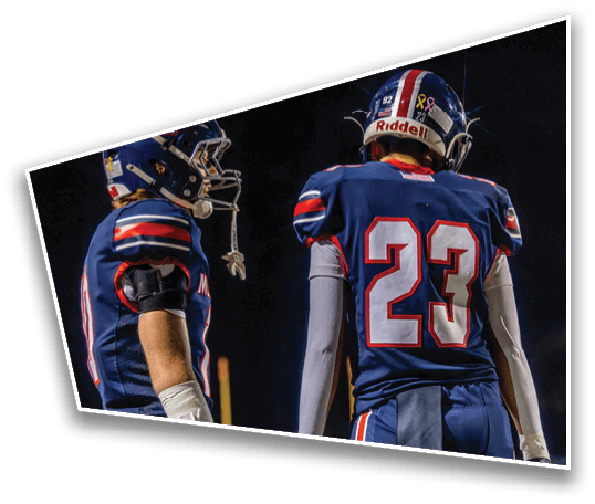 Two people wearing blue football uniforms with helmets stand facing each other on a field at night. Description generated by AI