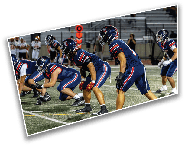A group of people in blue football uniforms and helmets are lined up on a field preparing for a play during a game. Description generated by AI