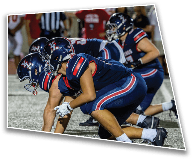Two people in athletic gear are crouched in a ready position on a sports field, preparing for a play. Description generated by AI