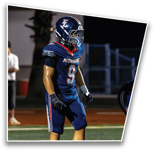 A person wearing a dark blue football uniform and helmet with a “Mustangs" logo stands on a field at night. Description generated by AI