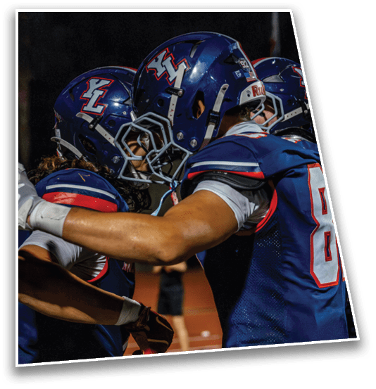 Two people in blue football uniforms and helmets are embracing on a field at night. Description generated by AI
