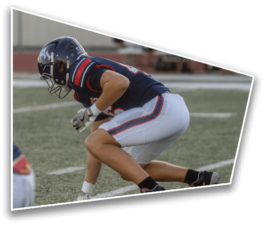 A person in a football uniform and helmet is crouched in a ready position on a football field. Description generated by AI